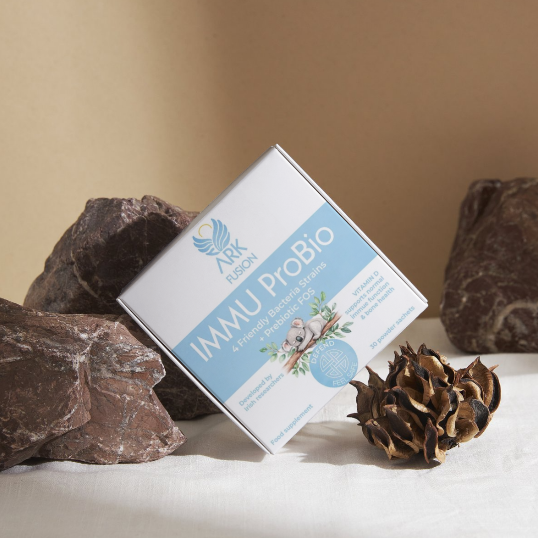 ARK Fusion IMMU ProBio supplement box resting on natural stones. Label reads: '4 Friendly Bacteria Strains + Prebiotic FOS. Developed by Irish researchers. Vitamin D supports immune function, teeth & bone health.' 30 powder sachets. Food supplement.
